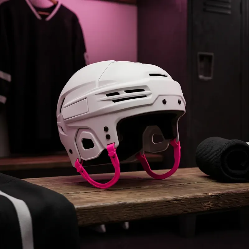 White hockey helmet with magenta ear loops on a locker room bench